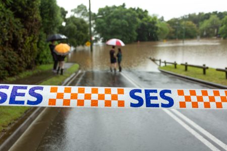 Windsor, Australia - March 22, 2021; SES (State Emergency Services) tape stretched across a flooded road as locals look on. Extreme weather caused flooding not seen in over 50 years.